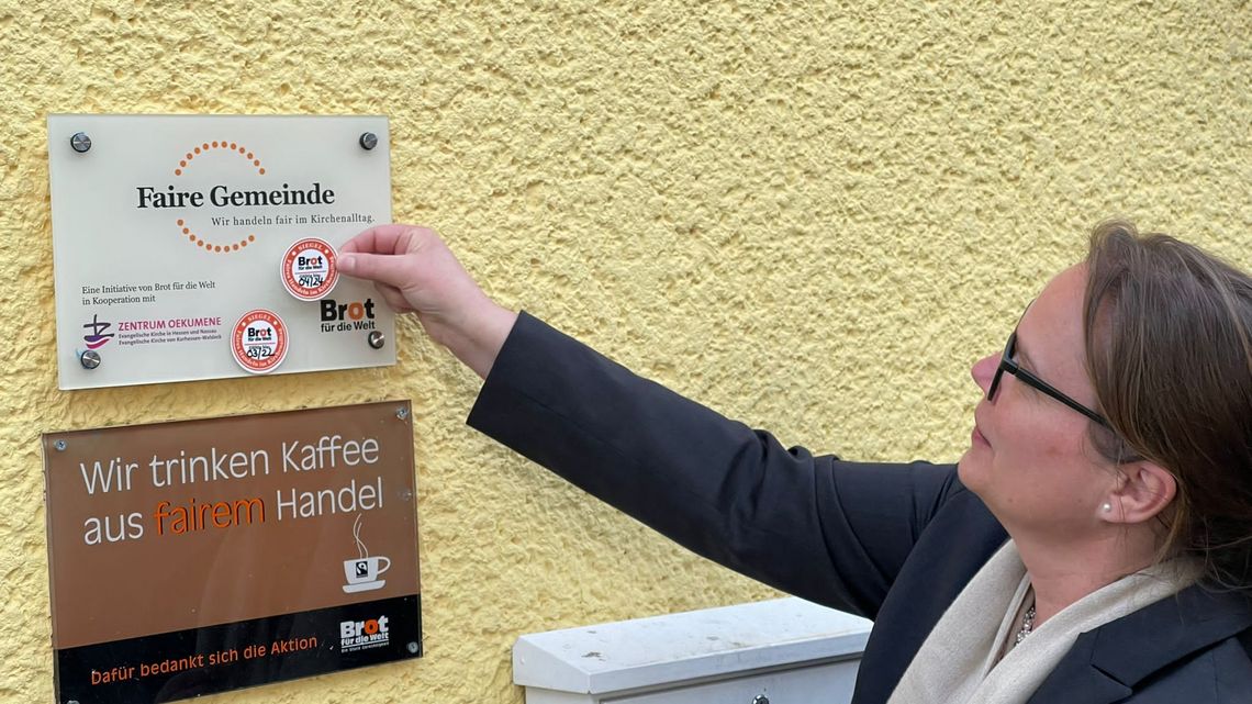 Brigitte Molter bringt das neue Siegel auf dem Faire Gemeinde-Schild an.