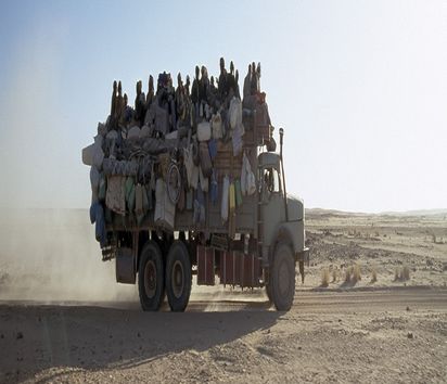 Ein Lastwagen der mit Menschen und Gepäck beladen ist fährt durch die Wüste
