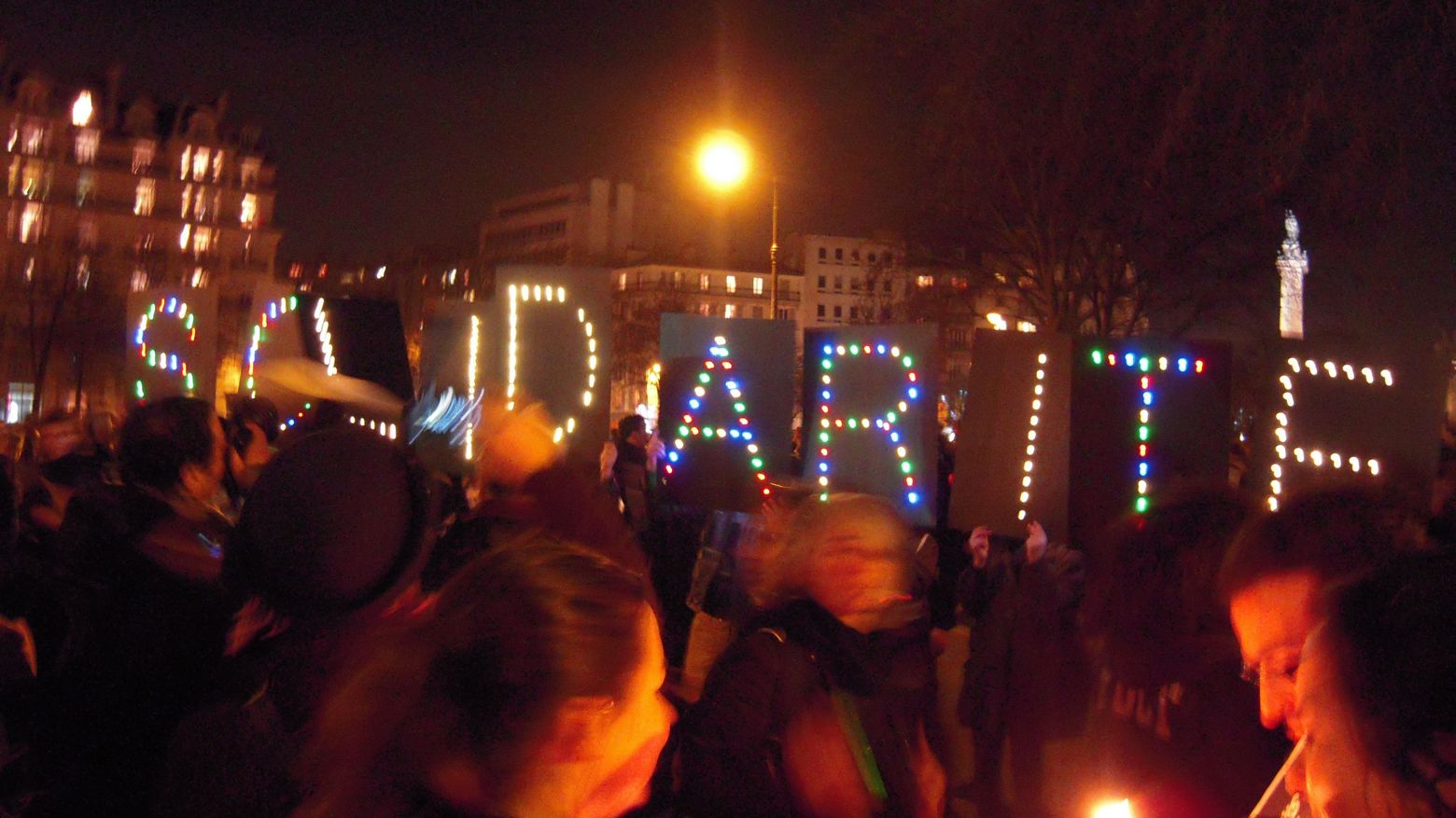 Menschen auf einer Demonstration halten den beleuchteten Schriftzug SOLIDARITE hoch.