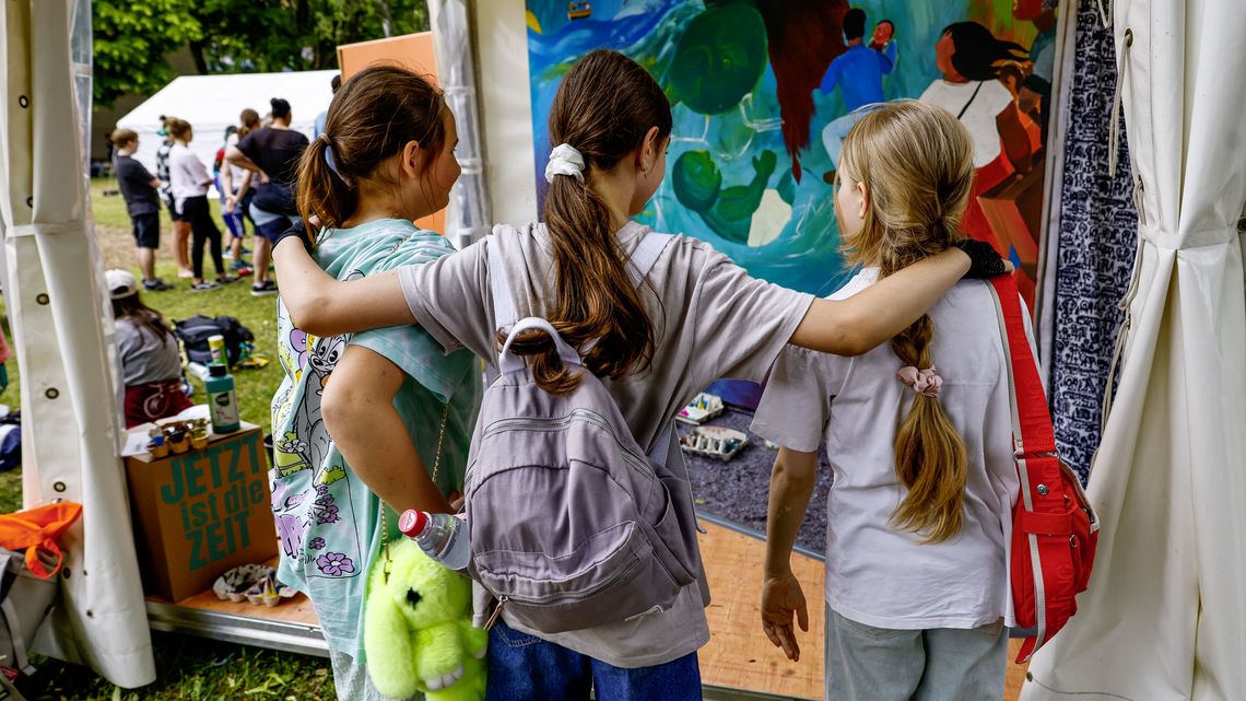 drei Kinder vor einem gemalten Bild am Stand der Brot für die Welt Jugend