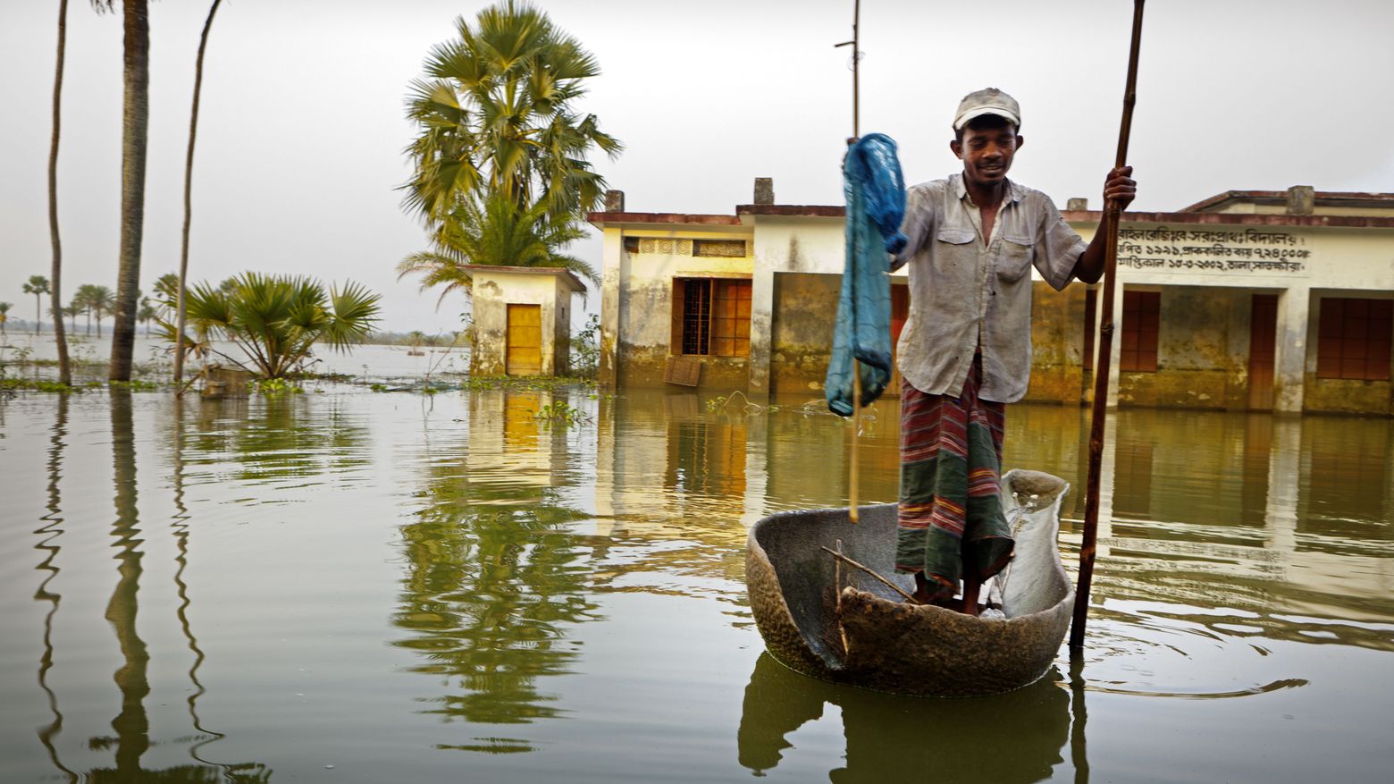 Fischer mit Holzboot vor überfluteter Landschaft in Bangladesch.